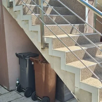 Sanierte Außentreppe mit beigem Steinteppich und Edelstahlgeländer