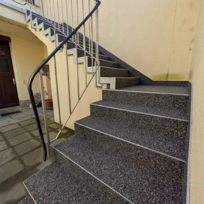 Sanierte Außentreppe mit dunklem Steinteppich und Handlauf